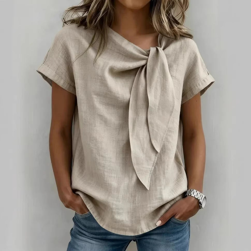 Woman wearing a beige top with a scarf tied around her neck against a plain background