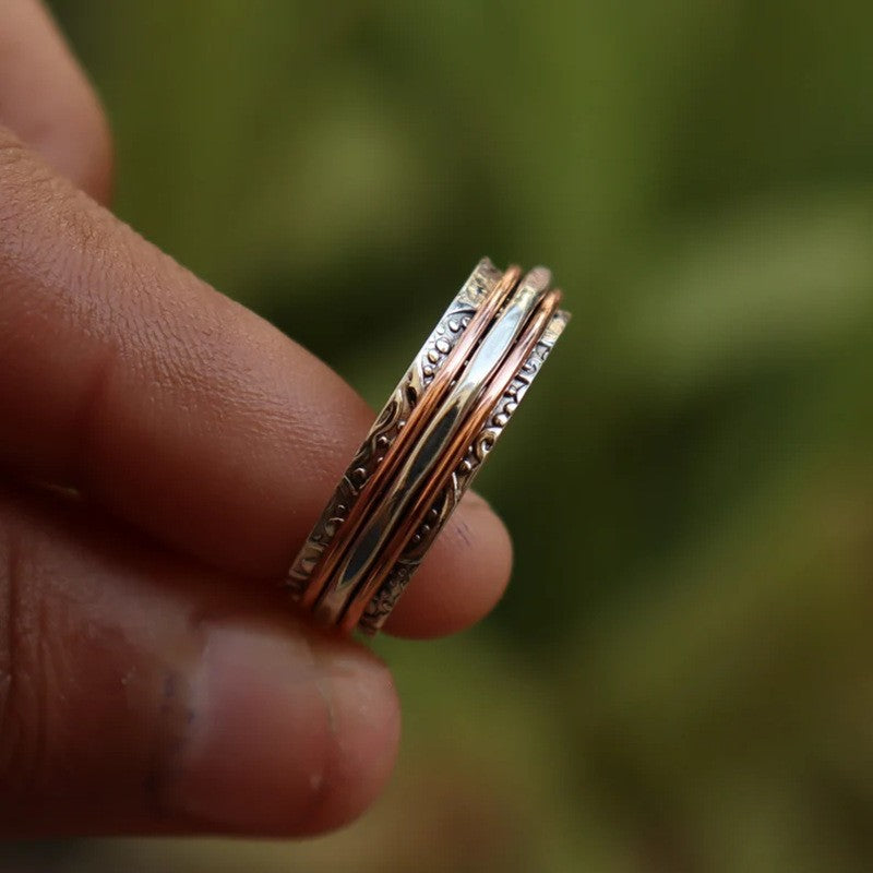 Three gold rings stacked on a finger with a blurred green background