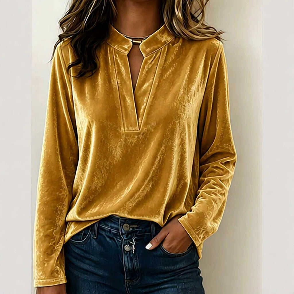 A woman wearing a long-sleeve velvet top in mustard yellow with a split V-neckline, paired with dark blue jeans, shown against a plain light background.