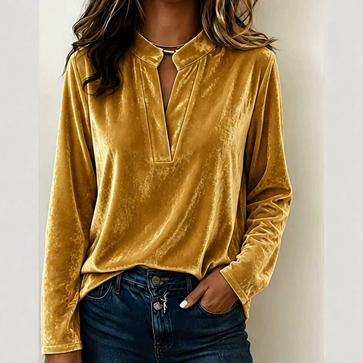 A woman wearing a long-sleeve velvet top in mustard yellow with a split V-neckline, paired with dark blue jeans, shown against a plain light background.