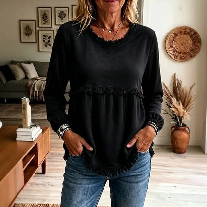 Woman wearing a black top with ruffled details in a living room setting.
