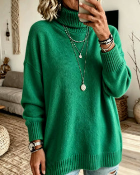 A woman wearing a bright green oversized turtleneck sweater, taking a mirror selfie in a cozy living room setting.