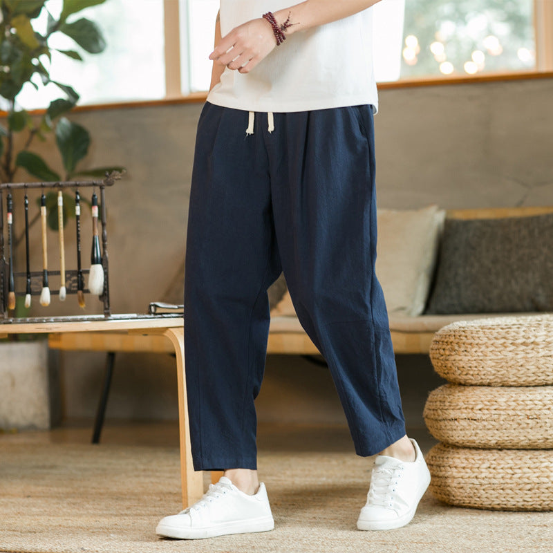 Person wearing navy blue pants and white sneakers in a room with a couch and plants.