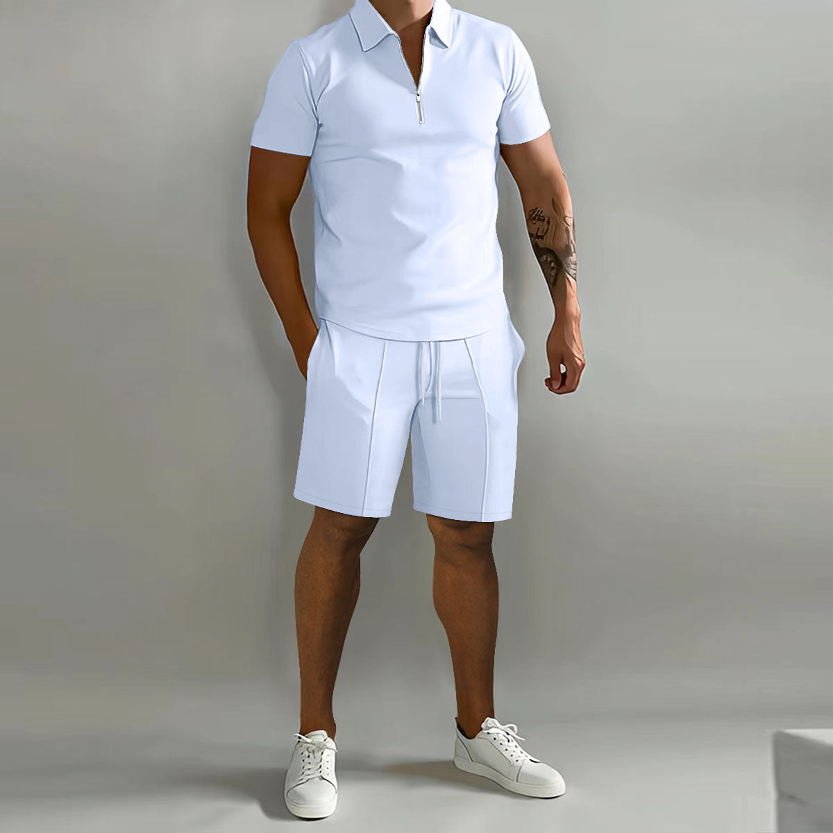 A man modeling a light blue short-sleeve polo shirt and matching light blue shorts, paired with white sneakers, against a plain light gray studio background.