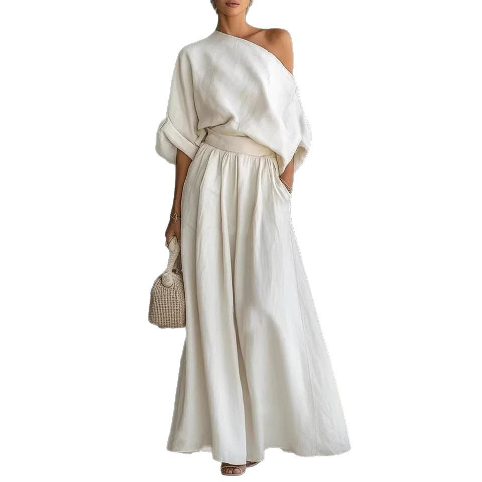 Woman wearing a white one-shoulder dress holding a woven handbag on a white background
