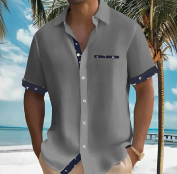A man wearing a gray short-sleeve button-up shirt with navy blue patterned trim on the collar, cuffs, and chest pocket, set against a tropical beach background with palm trees and ocean.