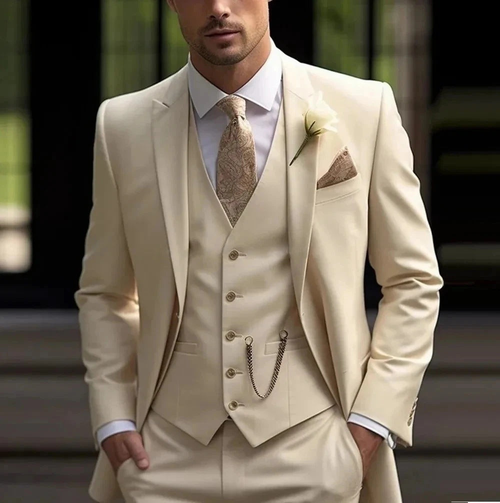 Man wearing a beige suit with a tie and pocket square, standing outdoors.