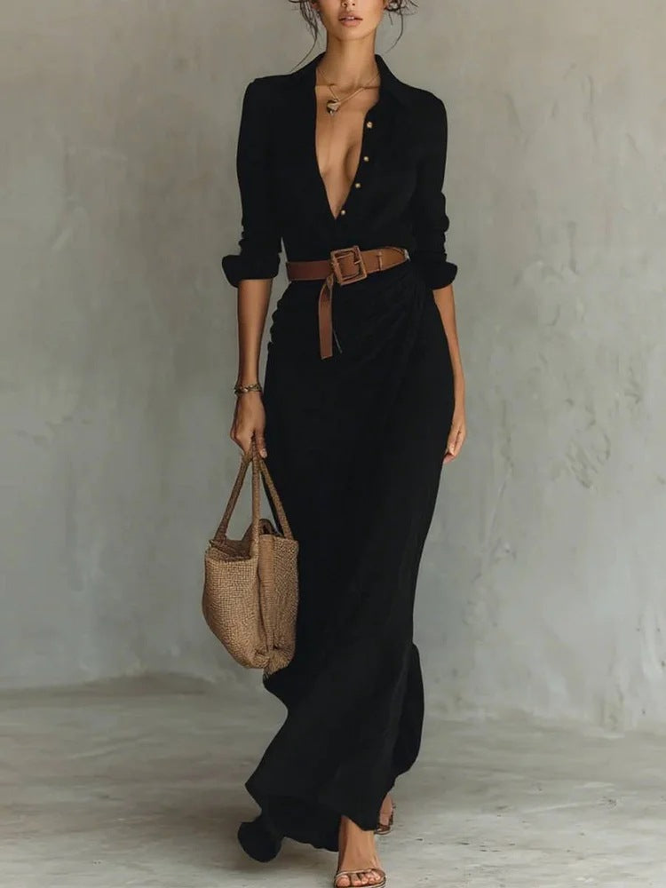 Woman wearing a black dress with a brown belt and holding a woven bag against a plain background