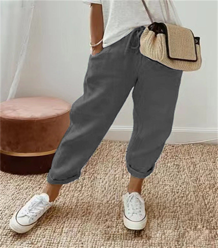 Person wearing gray pants and white sneakers with a beige bag, standing on a carpeted floor.