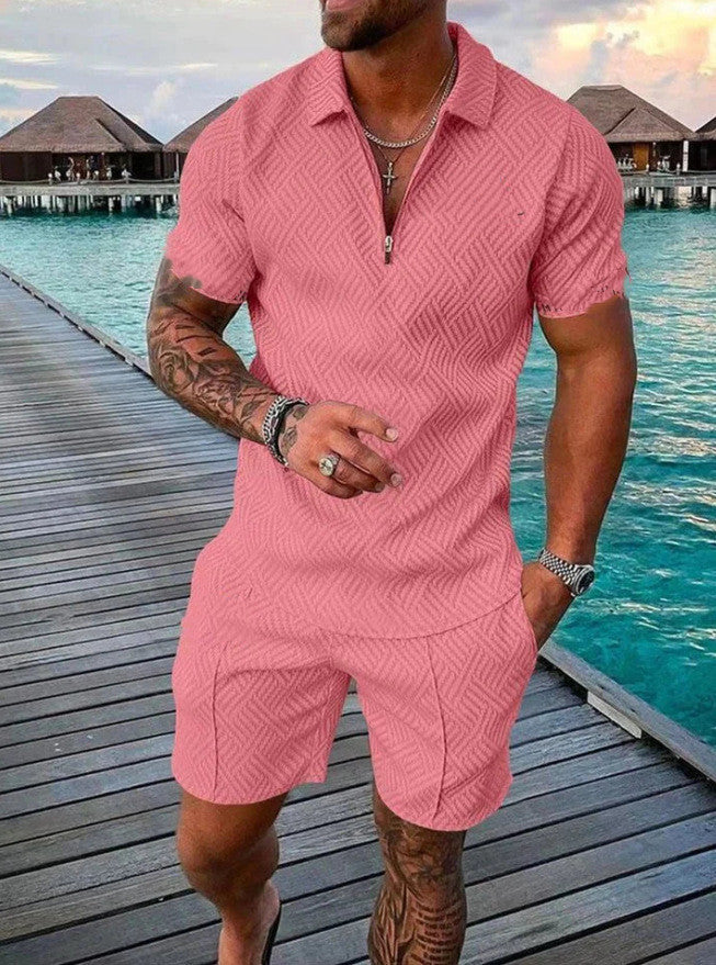 Man wearing a pink textured outfit standing on a wooden dock by water.