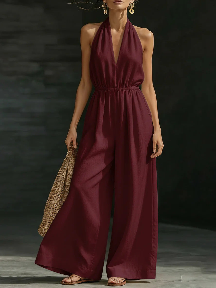 Woman wearing a burgundy jumpsuit holding a woven bag against a dark background