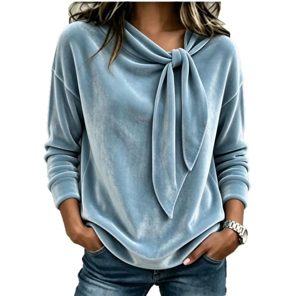 A woman wearing a light blue long-sleeve knit top with a knotted tie neckline, paired with blue jeans, shown against a plain white background.