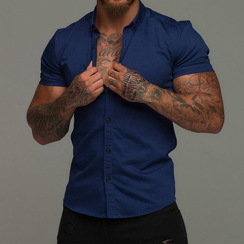 Man wearing a blue shirt with tattoos on his arms against a gray background