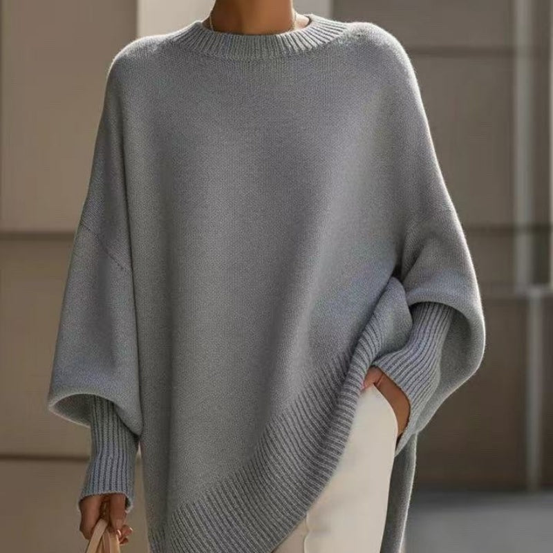 A person wearing a light gray oversized knit sweater with wide batwing sleeves and a crew neckline, paired with off-white pants.