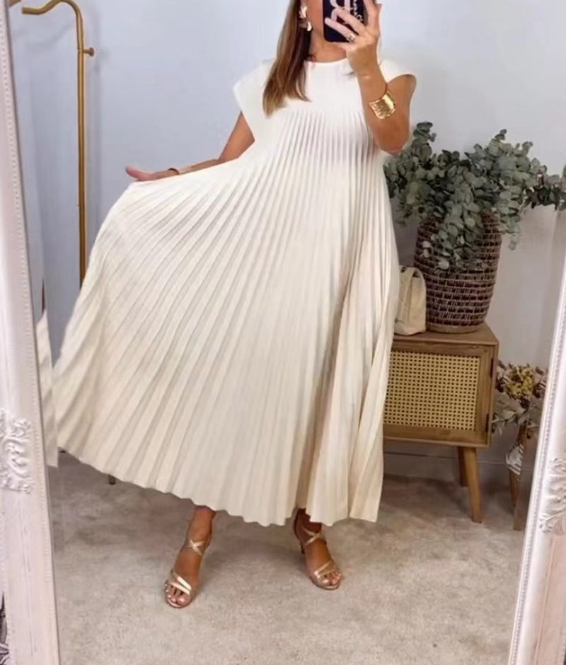 Person wearing a white pleated dress in a room with a plant and wooden cabinet.