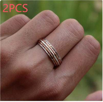 Hand wearing two gold rings with a blurred green background