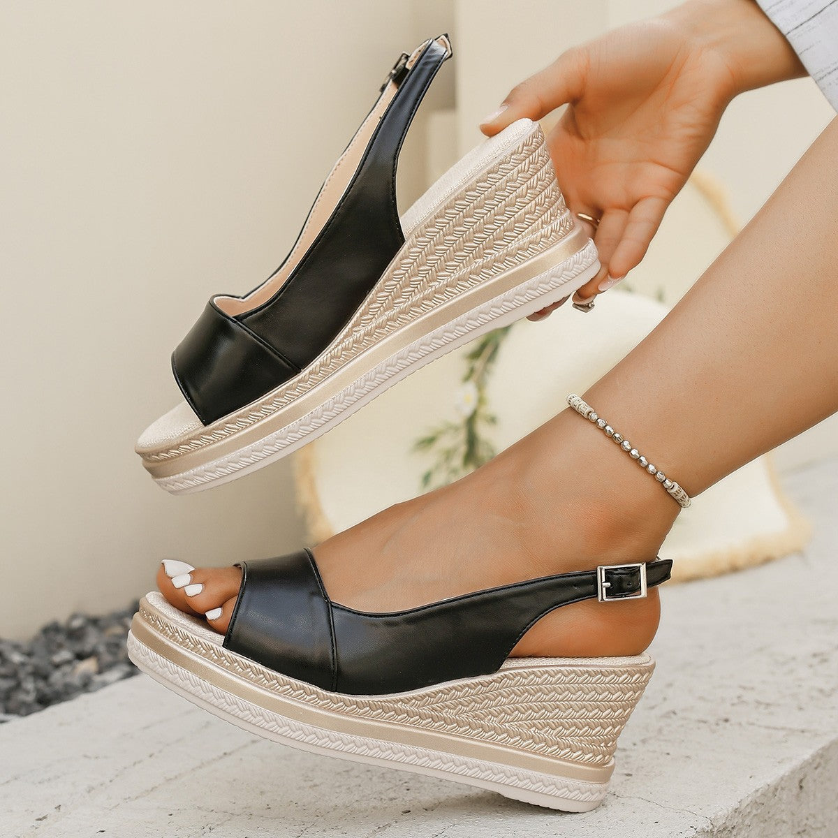 Black wedge sandals with white soles worn by a person on a light background