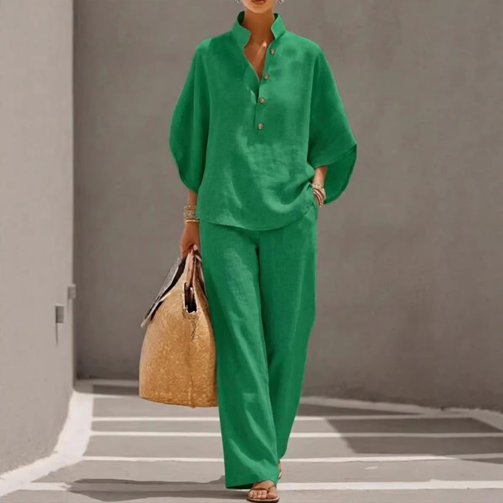 Person wearing a green outfit holding a straw bag against a gray wall.