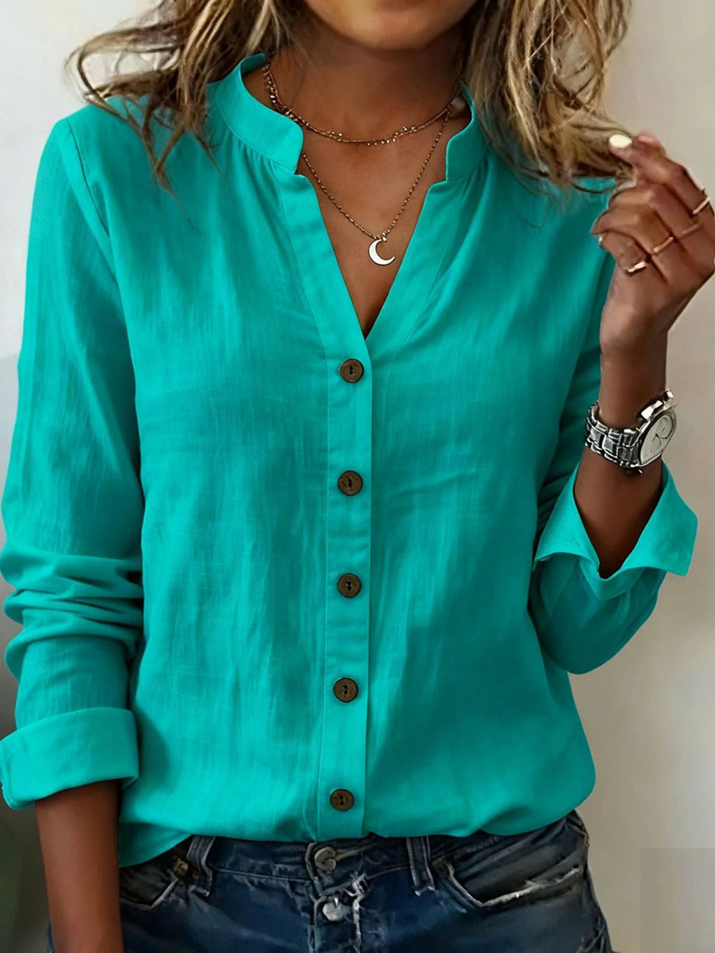 Person wearing a turquoise button-up shirt with rolled-up sleeves, accessorized with necklaces and a watch.