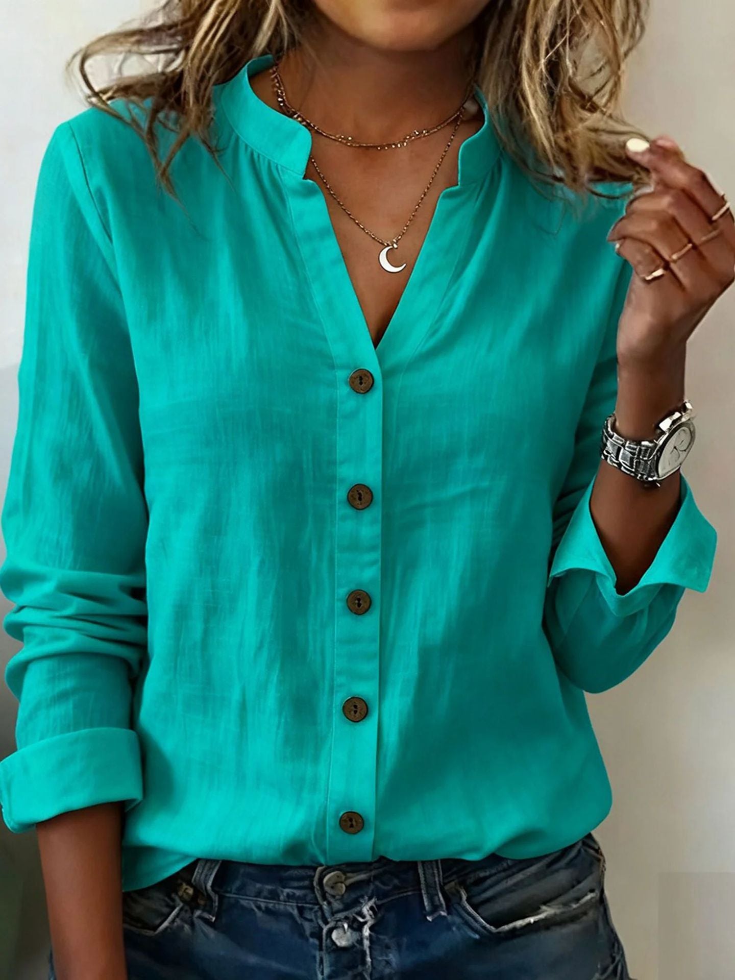 Person wearing a turquoise button-up shirt with rolled-up sleeves, accessorized with necklaces and a watch.