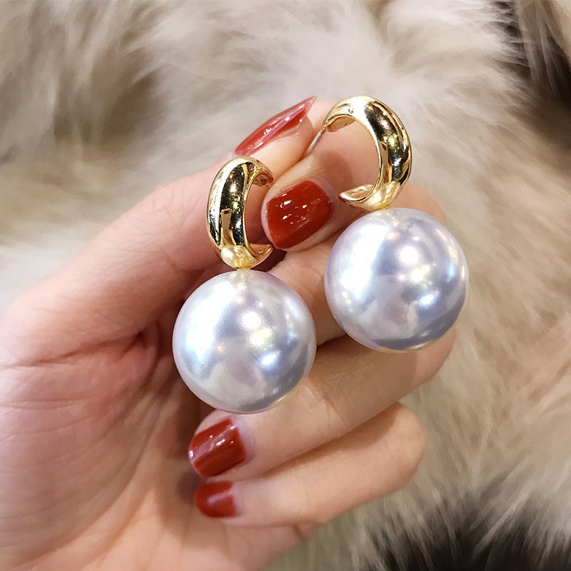 Gold and pearl earrings held by a hand with red nail polish against a fur background