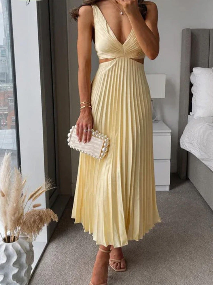 Woman in a yellow pleated dress holding a clutch in a room with a bed and lamp.