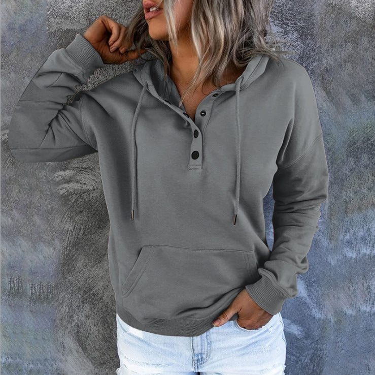 Person wearing a gray hoodie with button details against a textured wall.