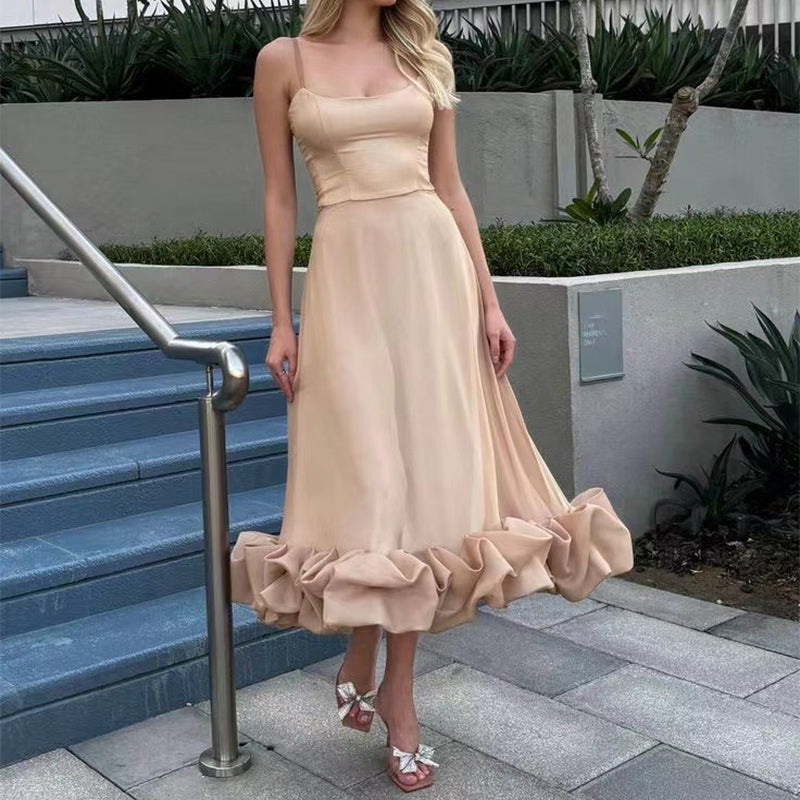 Woman in a beige dress with ruffled skirt standing on outdoor steps.