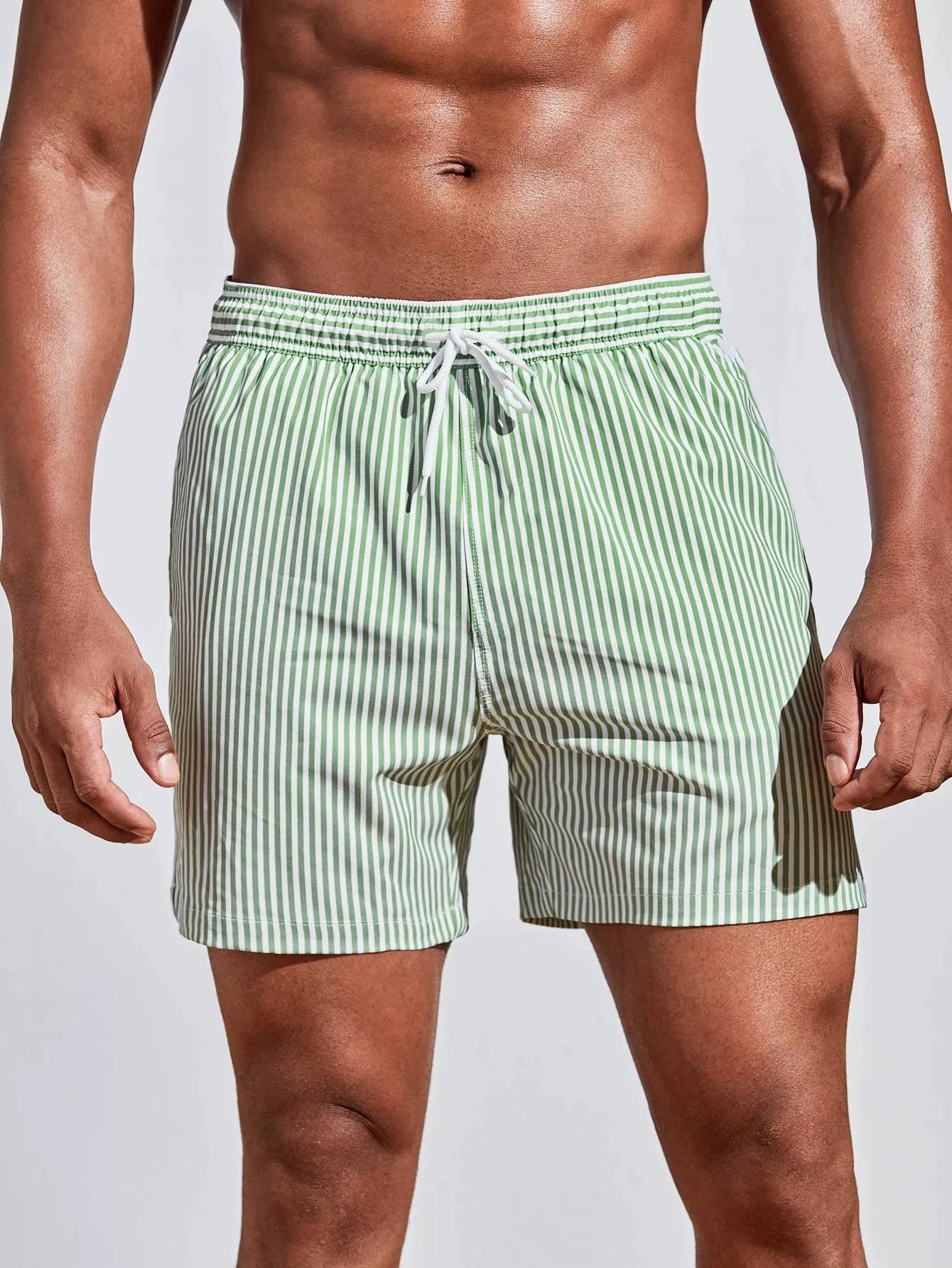 Green striped swim shorts worn by a person on a plain background