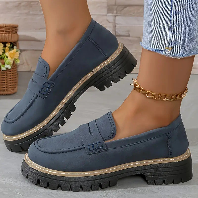 Blue loafers worn with denim jeans on a neutral background