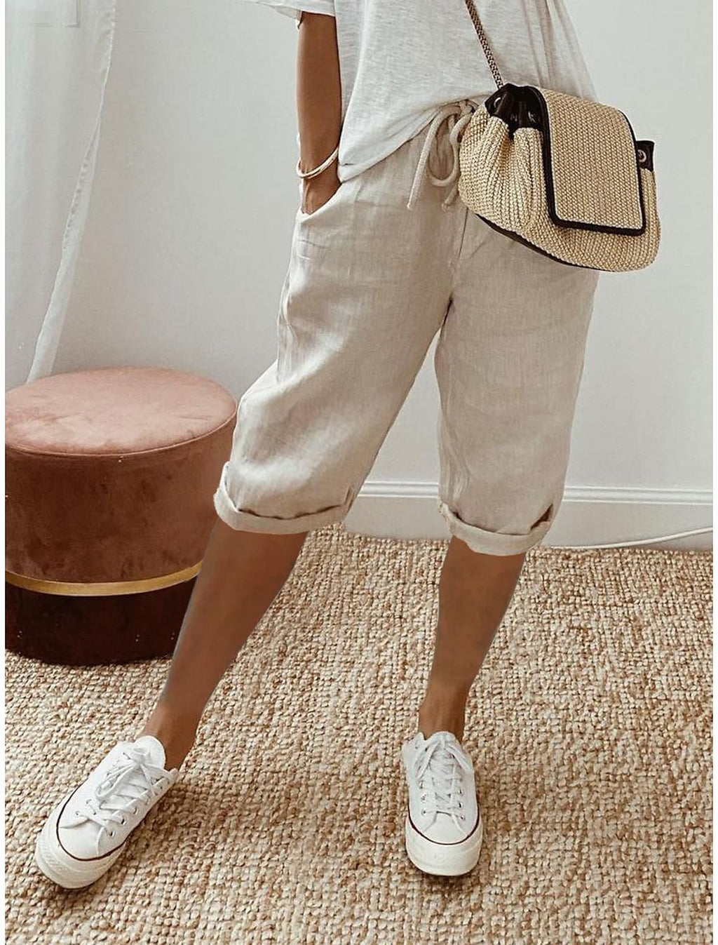 Person wearing beige shorts, white sneakers, and a straw bag on a carpeted floor.