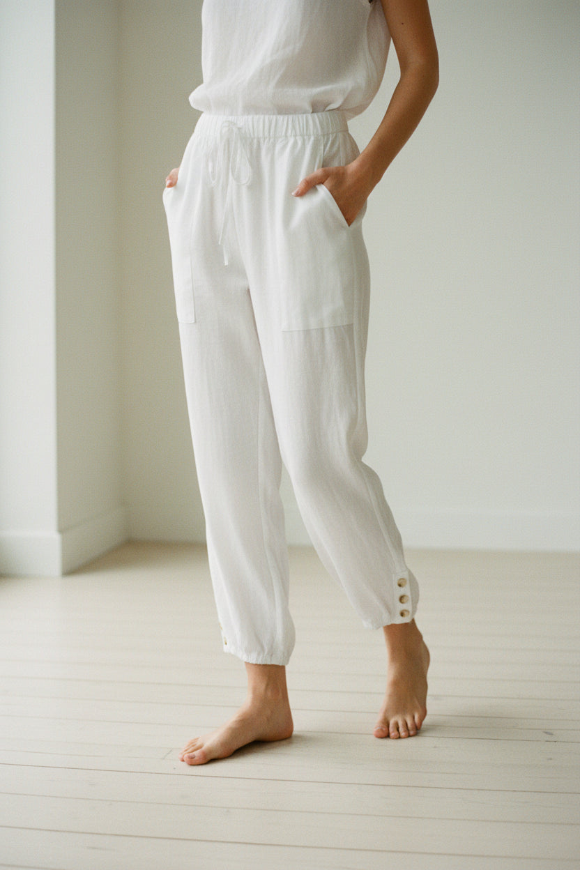 White pants with button details worn by models on a light wooden floor.
