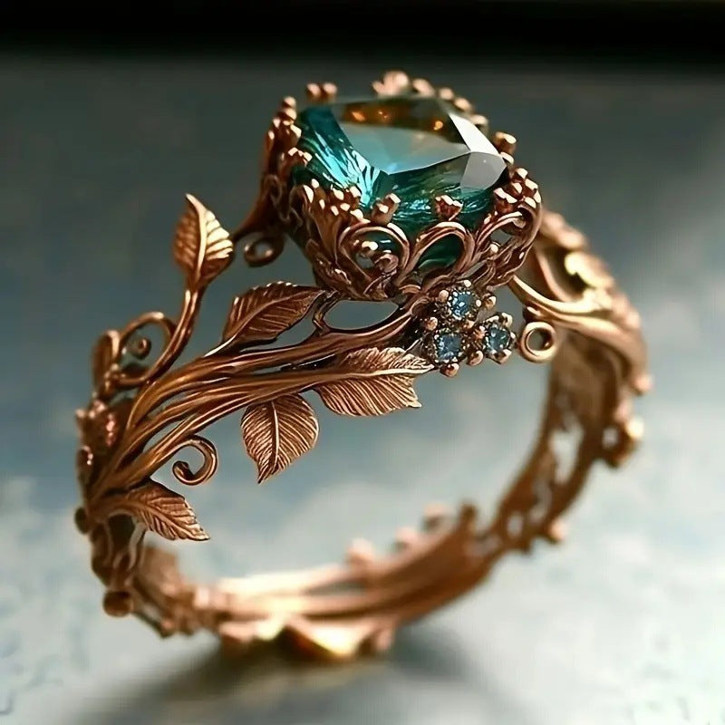 Ornate ring with green gemstone and rose gold leaf design on a blurred background