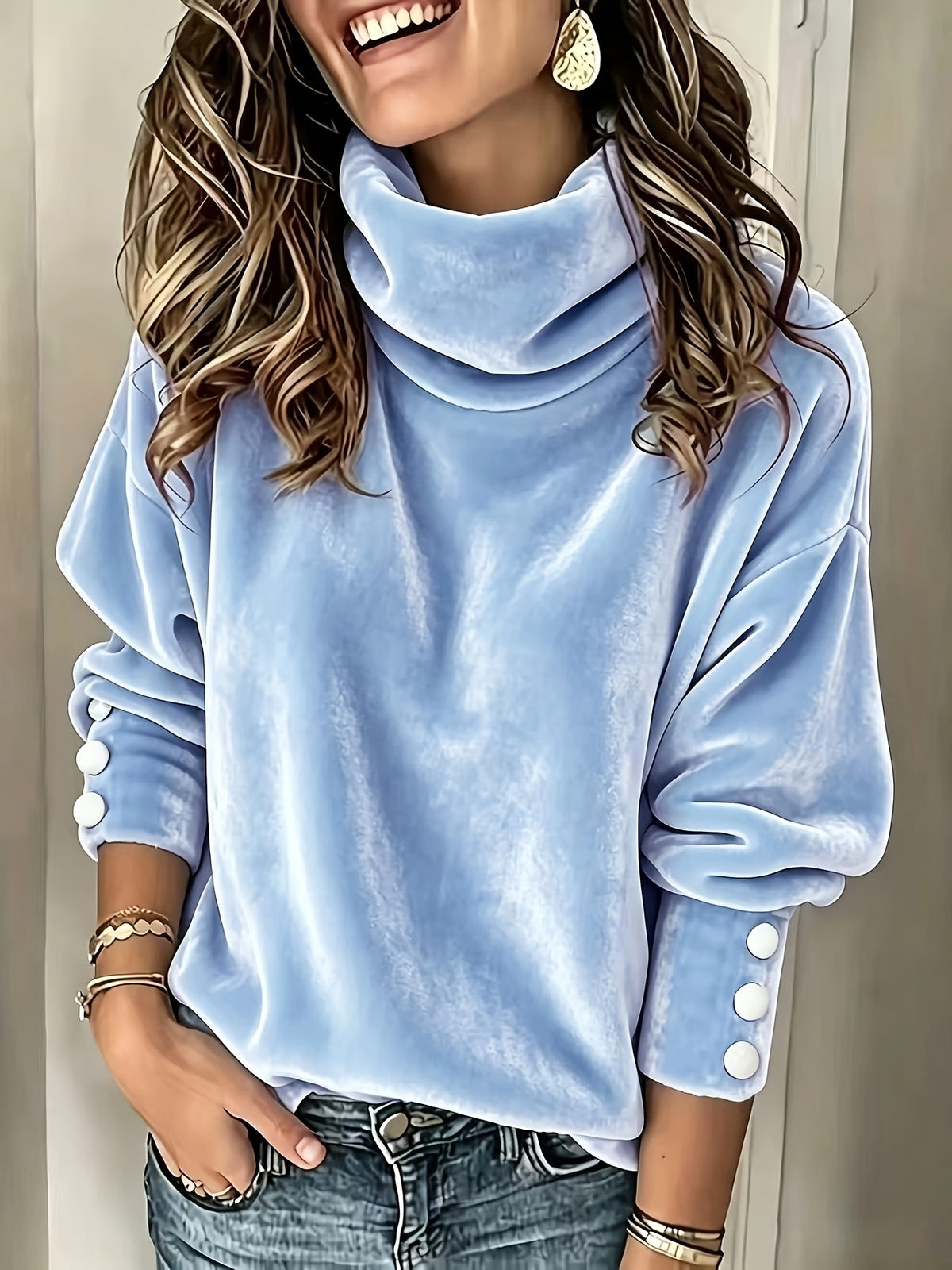 A woman wearing a light blue velvet cowl-neck sweatshirt with decorative white buttons on the sleeves, paired with blue jeans.