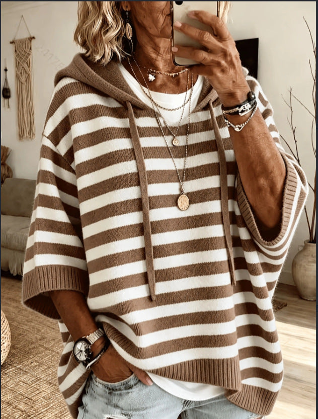 A woman takes a mirror selfie wearing a brown and off-white horizontally striped knit hoodie with wide sleeves and ribbed cuffs and hem, paired with light-wash jeans and layered necklaces.