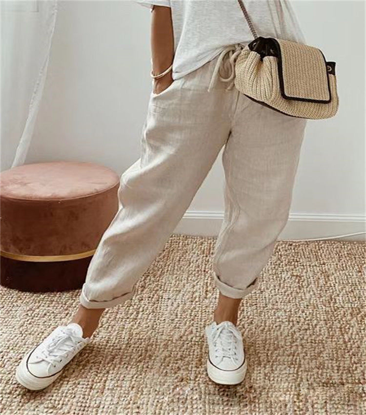 Person wearing beige pants and white sneakers with a straw bag on a neutral background