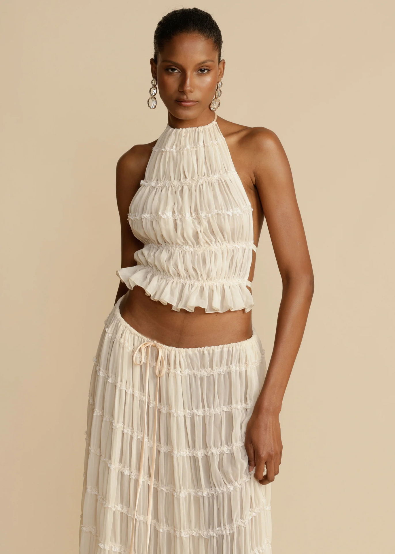 Woman wearing a white ruffled top and skirt set against a beige background