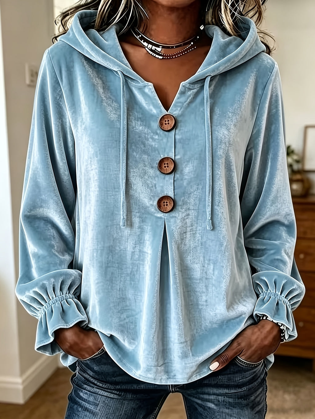 A woman wearing a light blue velour hooded pullover top with three brown buttons down the front, paired with dark blue jeans.