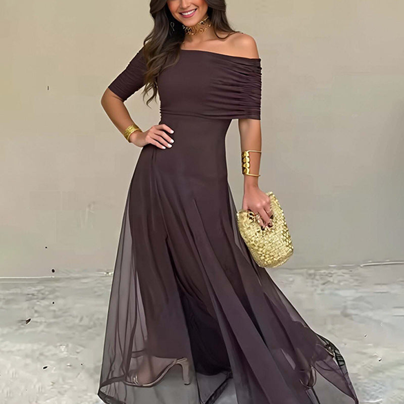 Woman wearing a brown off-shoulder dress holding a gold handbag against a plain background