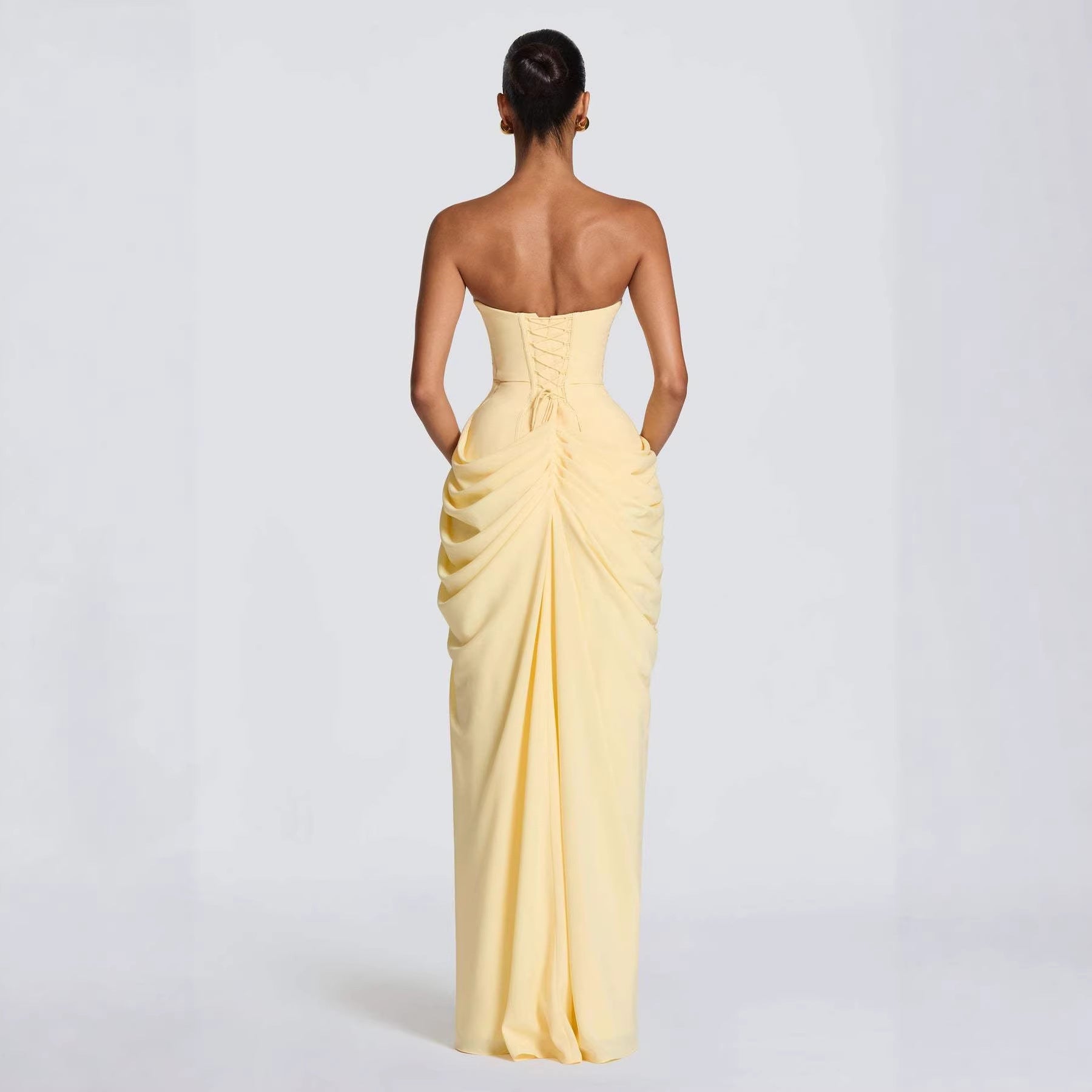 Woman wearing a yellow strapless gown with ruched detailing on a white background