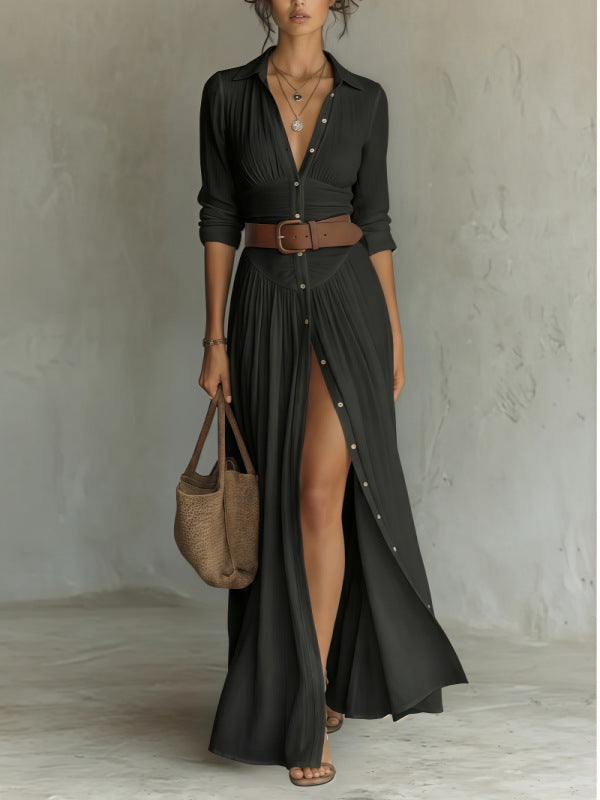 Woman wearing a long black dress with a belt and holding a woven bag against a plain background
