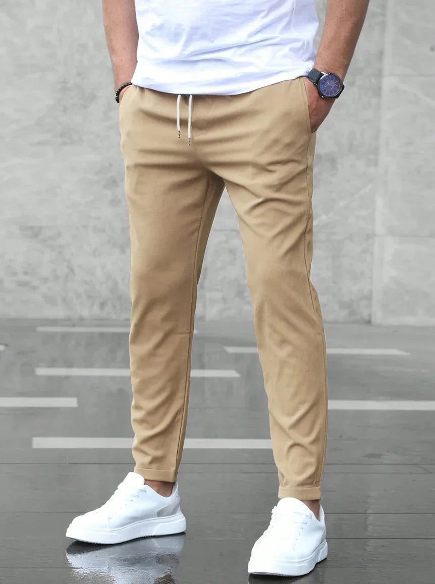 Person wearing beige jogger pants and white sneakers on a gray concrete floor.