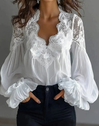 A woman wearing a white long-sleeve blouse with intricate lace detailing around the deep V-neck and sheer balloon sleeves, paired with dark jeans.
