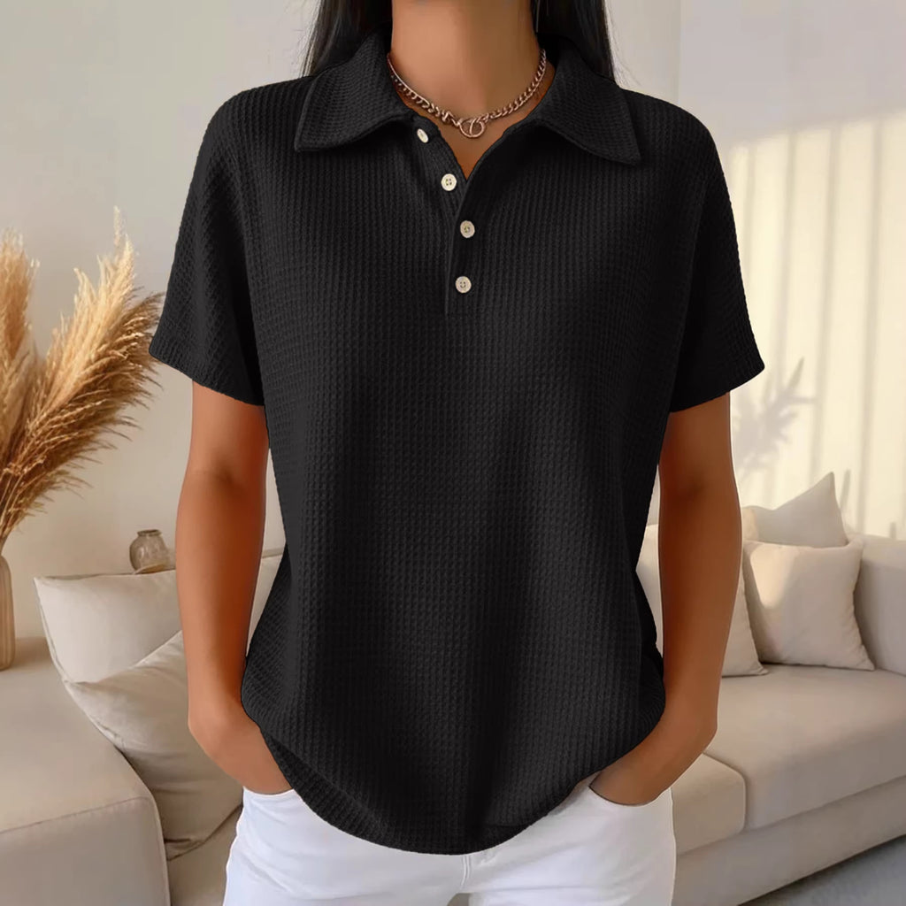 Person wearing a black short-sleeve shirt with white buttons in a living room setting.