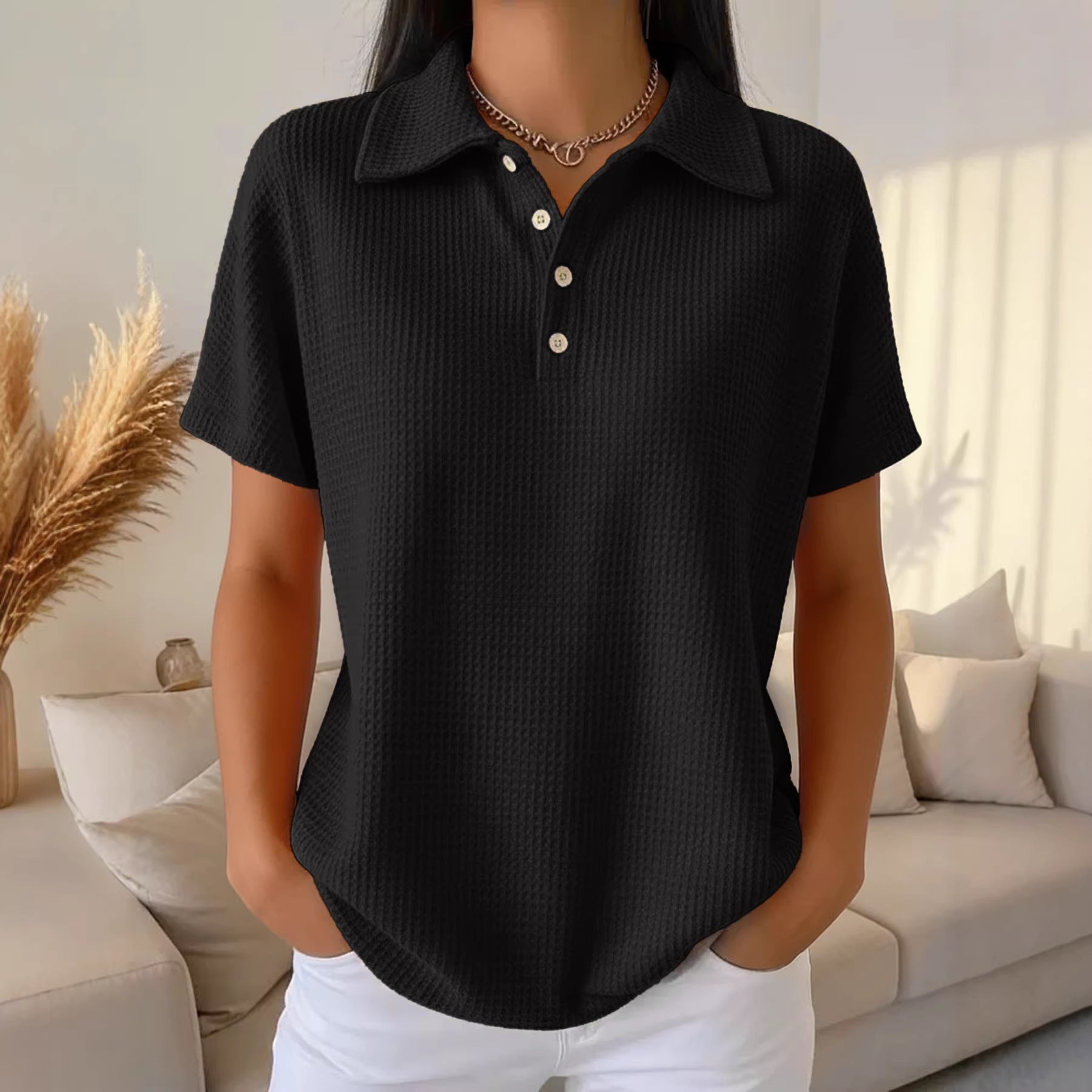 Person wearing a black short-sleeve shirt with white buttons in a living room setting.