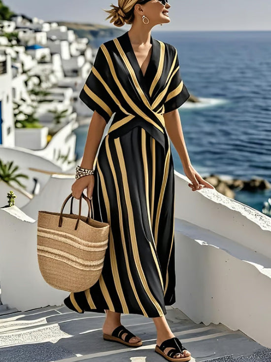 Woman in a black and gold dress with a straw bag standing on a balcony overlooking the ocean.
