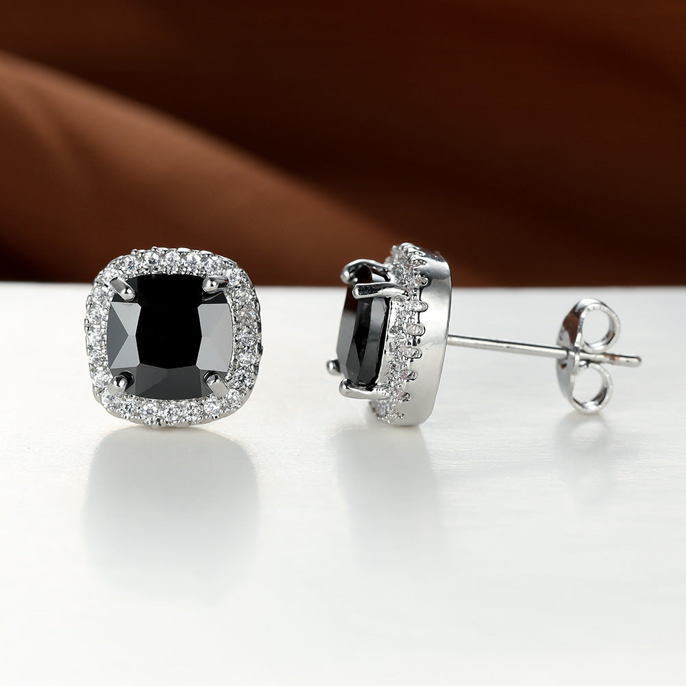 Black gemstone earrings with silver prongs on a reflective surface