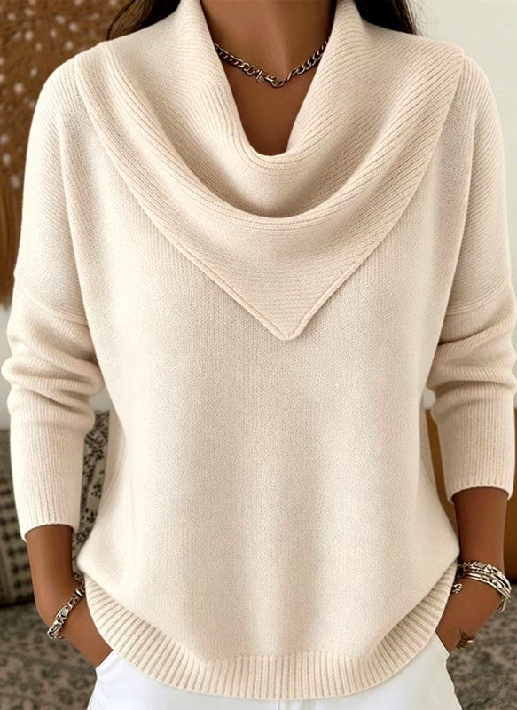 A woman wearing a cream-colored cowl neck knit sweater with long sleeves and a ribbed hem, paired with white pants and silver jewelry.