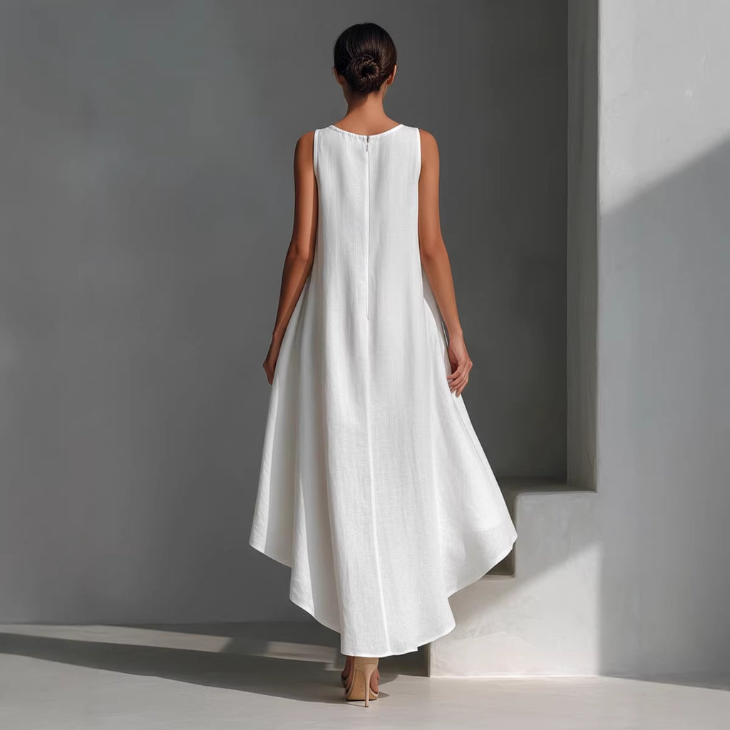Woman wearing a white dress standing against a gray wall.