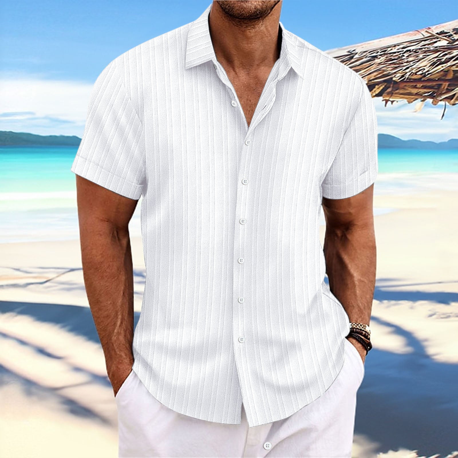 Man wearing a white striped shirt and white pants standing on a beach with a clear blue sky.